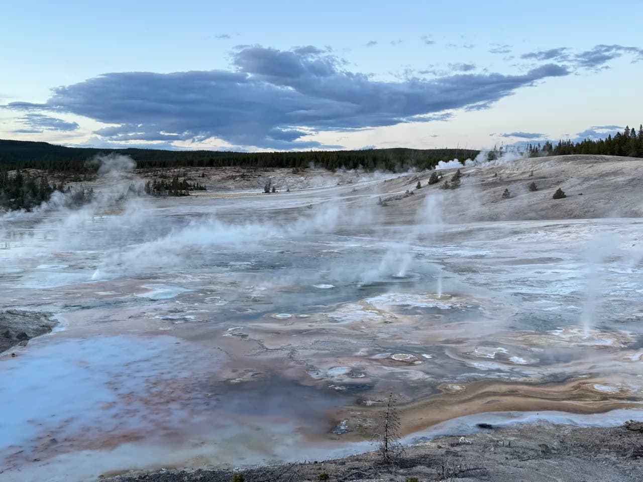Wide geothermal basin with steam rising beneath an open sky.