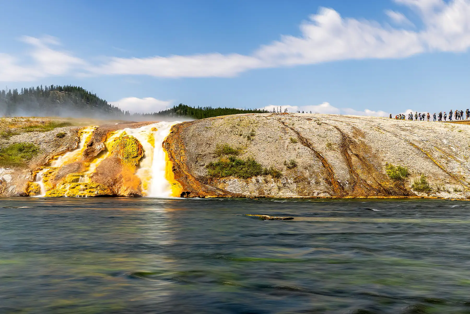Geothermal terraces beside a river under a blue sky.