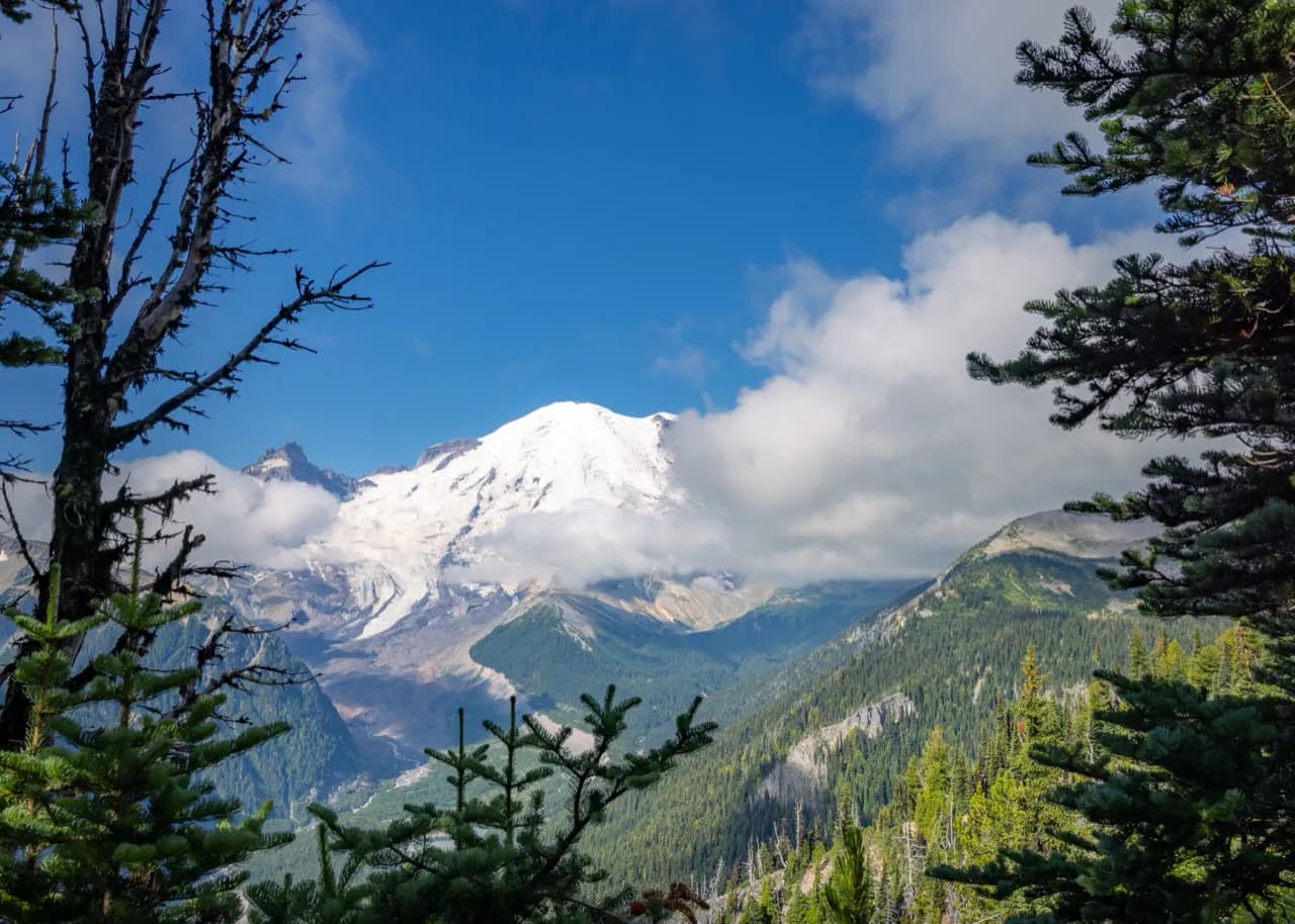 Mount Rainier beneath passing clouds and a clear blue sky.