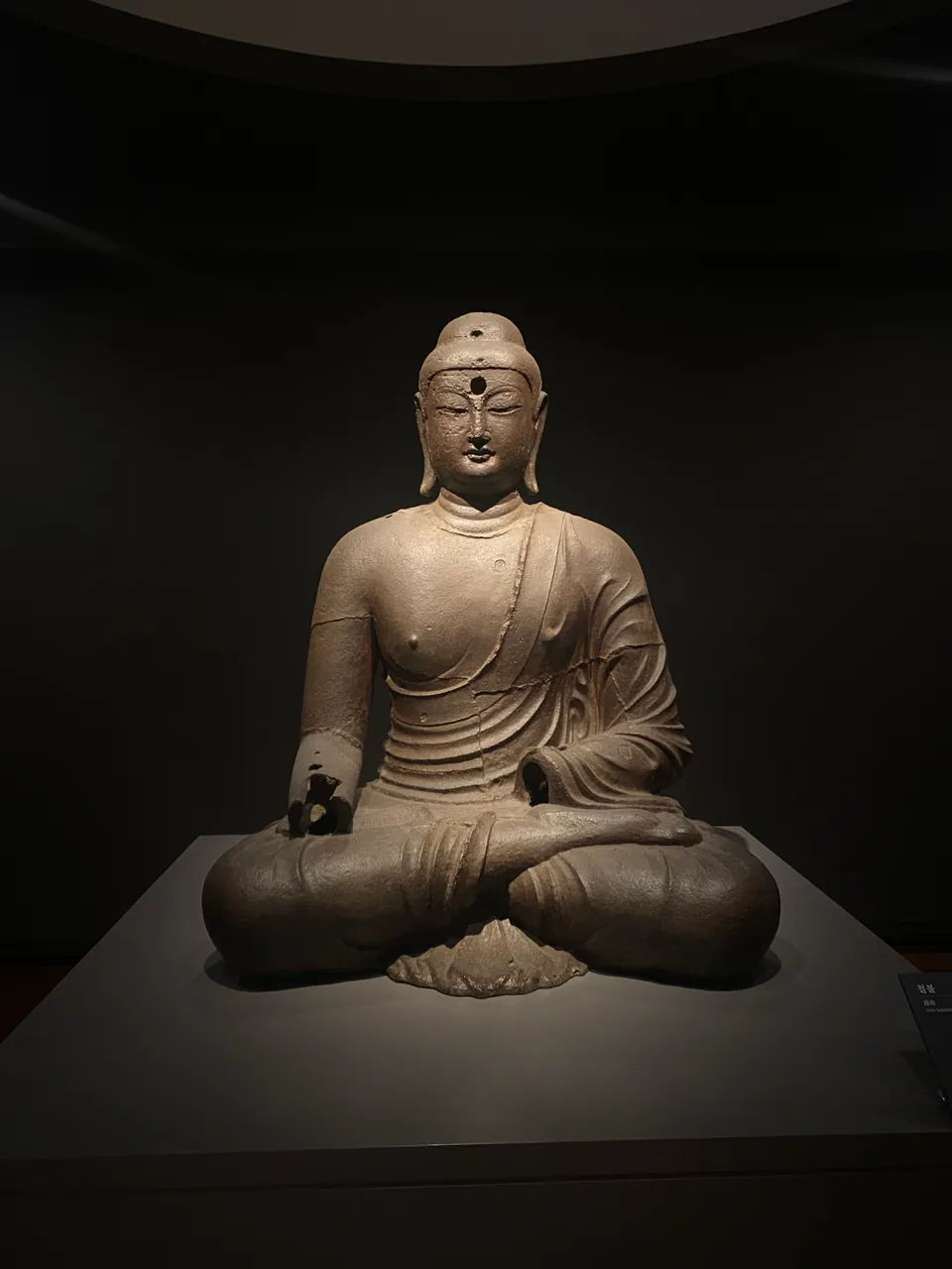 Historic seated Buddha sculpture displayed in a dark museum gallery.